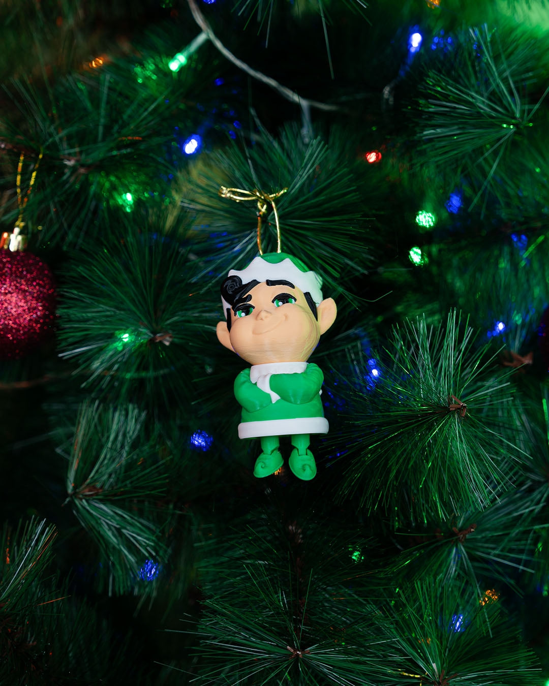 Christmas elf ornament hanging from its gold cord on a lit Christmas tree, legs dangling