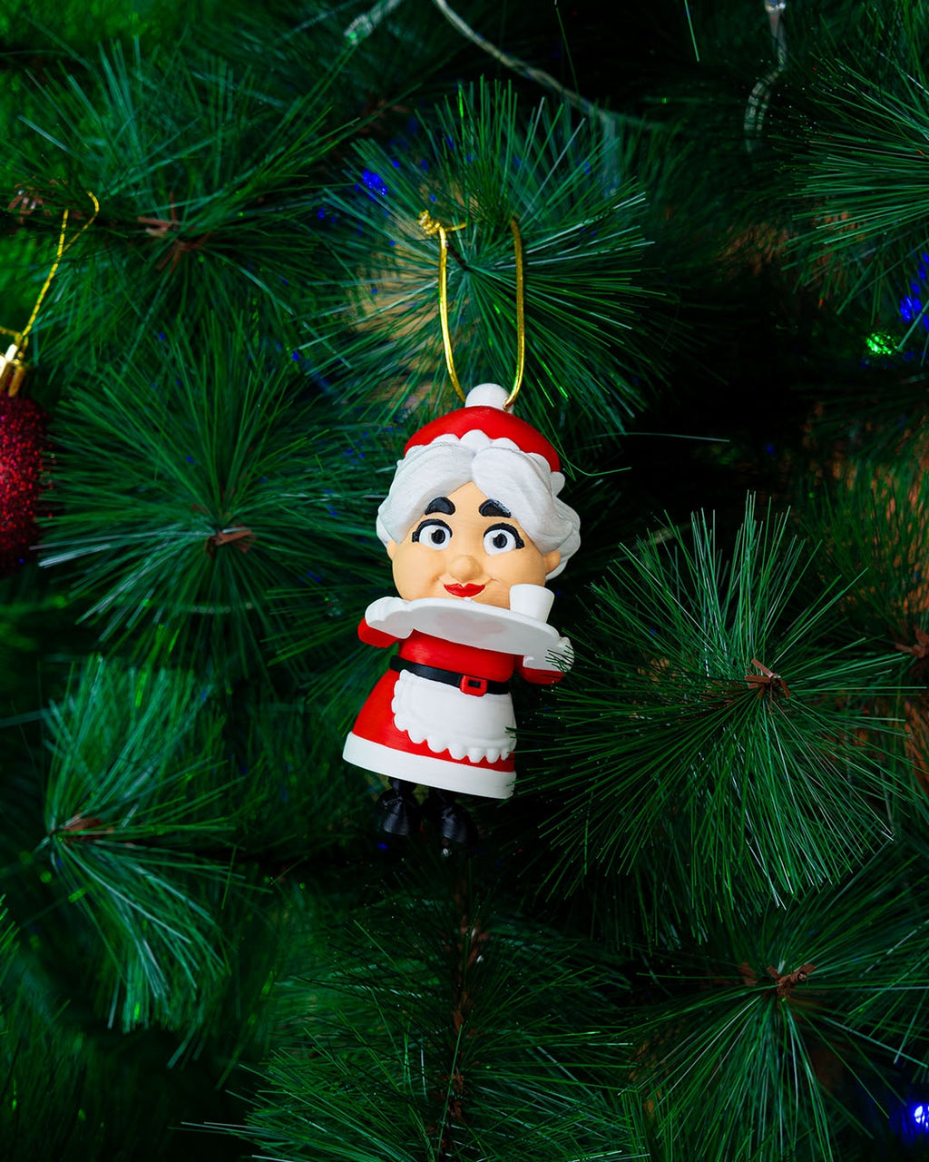 Mrs. Claus Christmas ornament hanging from its gold cord on a Christmas tree, legs dangling