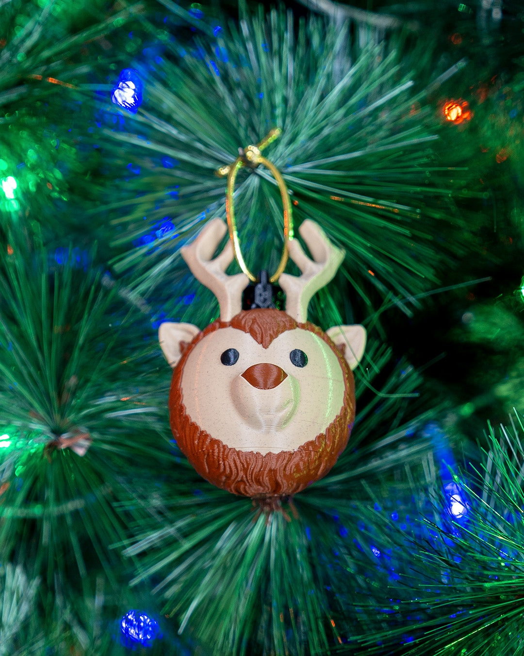 Reindeer Head Christmas ornament hanging from a branch of a lit Christmas tree, seen from a slight angle