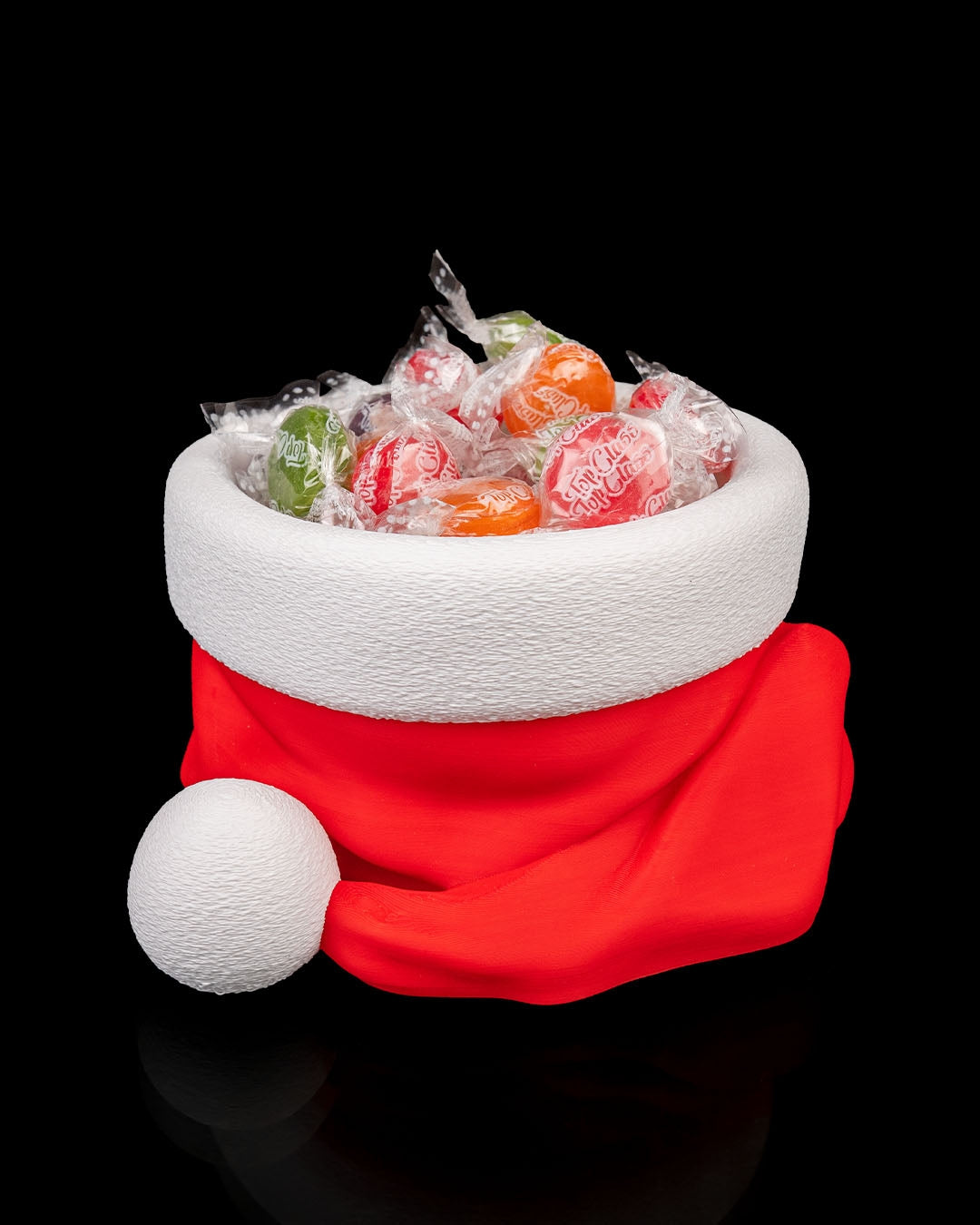 Santa hat candy bowl, 3D printed, red hat with a textured white brim and pom-pom, filled with wrapped hard candy, on a black background