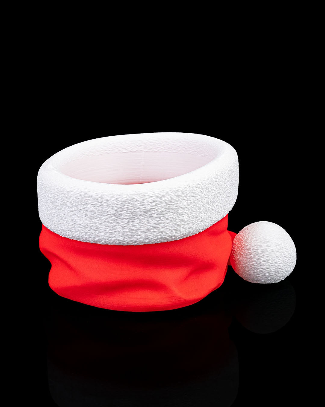 Santa hat candy bowl empty, red hat with textured white brim and pom-pom, three-quarter view on black background