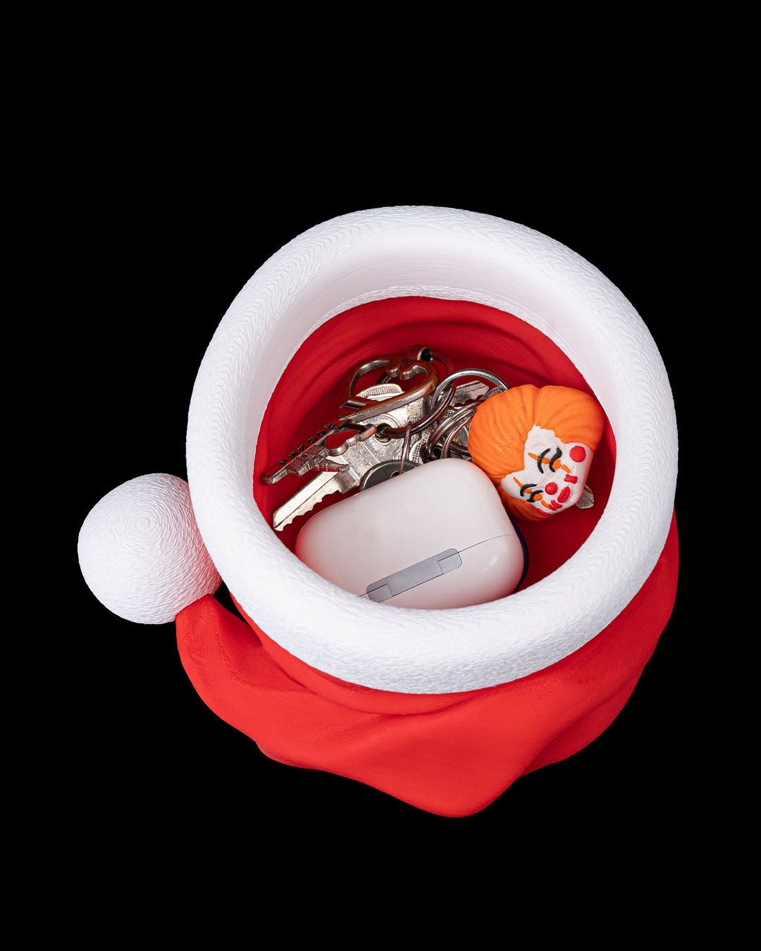 Santa hat candy bowl holding keys and AirPods, red hat with white brim and pom-pom, on black background