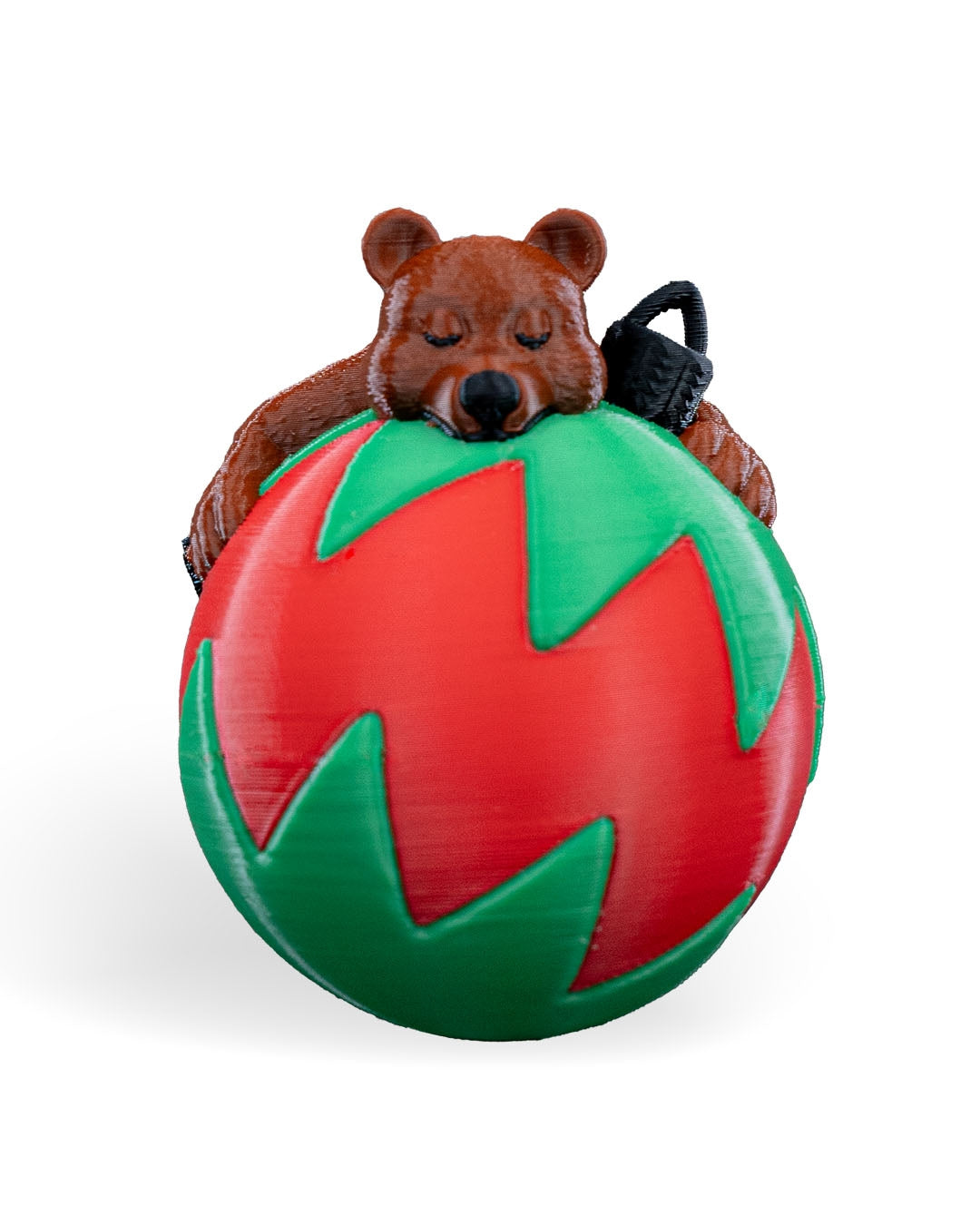 Sleeping Bear Christmas ornament, 3D printed, front view: brown bear asleep on a red ball with a green zigzag pattern, on a white background